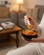 A complete 15-piece ceramic soup set displayed in a kitchen setting, featuring one large scalloped serving bowl, six small individual soup bowls, a golden metal storage stand, and seven white serving spoons. The set is available in six colors: black, dark gray-blue, navy blue, emerald green, beige/nude, and light mint green, all highlighted with an elegant gold rim.