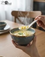 A complete 15-piece ceramic soup set displayed in a kitchen setting, featuring one large scalloped serving bowl, six small individual soup bowls, a golden metal storage stand, and seven white serving spoons. The set is available in six colors: black, dark gray-blue, navy blue, emerald green, beige/nude, and light mint green, all highlighted with an elegant gold rim.