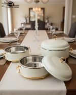 Set of three black insulated hot pot casseroles with gold trim and loop handles, sitting on a wooden dining table with a formal place setting.