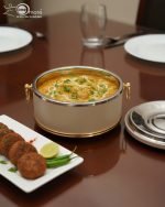 Set of three black insulated hot pot casseroles with gold trim and loop handles, sitting on a wooden dining table with a formal place setting.