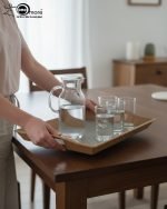 Set of three nesting fiber serving trays with non-slip textured surfaces and cut-out handles, displayed on a wooden dining table. The available colors are black, dark brown, grey, off-white, and rust-brown.