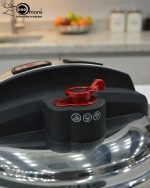 Top-down view of the O.M.S. Callacook 5-Litre Turkish pressure cooker lid. The lid features a sleek stainless steel and black plastic housing with two prominent red push buttons for the unique, easy-to-use locking and unlocking mechanism. A separate red lever near the edge controls the advanced pressure valve, highlighting the high-quality, modern design and superior safety features of this premium, imported Turkish cooker.