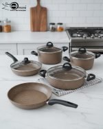 Falez 9-piece brown speckled granite non-stick cookware set displayed on a kitchen counter, featuring a fry pan, shallow casserole, and three deep pots with glass lids - Made in Turkey.