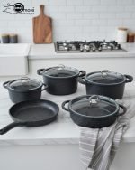 Falez 9-piece black granite non-stick cookware set including deep pots, shallow casserole, and fry pan with glass lids, displayed on a marble kitchen countertop.
