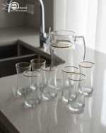 Pasabahce 7-piece clear glass water set featuring one jug and six glasses with elegant gold rims, displayed on a wooden dining table.