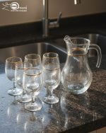 Pasabahce Turkish glass water set featuring 1 glass jug and 6 stemmed goblet glasses with elegant gold rims, arranged on a dining table.