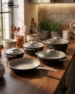 Falez 9-piece black granite non-stick cookware set including fry pan, shallow casserole, and three pots with glass lids and stainless steel handles, arranged on a wooden table.