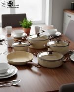 Falez 9-piece beige granite non-stick cookware set arranged on a kitchen surface, featuring three deep pots, one shallow casserole, and one fry pan with wood-effect handles and glass lids, made in Turkey.