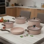Falez 9-piece pink granite non-stick cookware set including 3 cooking pots with lids, 1 shallow casserole with lid, and 1 frying pan displayed on a kitchen counter and dining table, demonstrating healthy low-oil cooking with steam rising from hot food.