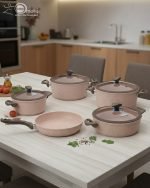 Falez 9-piece pink granite non-stick cookware set including 3 cooking pots with lids, 1 shallow casserole with lid, and 1 frying pan displayed on a kitchen counter and dining table, demonstrating healthy low-oil cooking with steam rising from hot food.