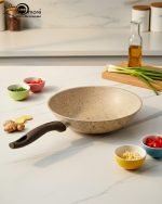 Falez beige granite non-stick wok pan made in Turkey, displayed on a marble kitchen counter with fresh ingredients, showing dynamic stir-fry cooking with shrimp and easy cleaning with a white cloth.