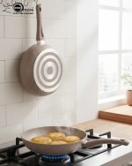 O.M.S premium granite non-stick fry pan made in Turkey, shown cooking vegetables with minimal oil usage and featuring a durable speckled beige finish.