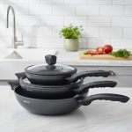 One More 24cm granite non-stick wok with glass lid and black silicon handle, displaying healthy low-oil cooking with fresh vegetables in the background.