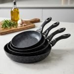 Stack of One More black granite non-stick cooking pots in four sizes (22cm, 24cm, 26cm, and 28cm) with ergonomic handles, displaying a premium speckled texture.