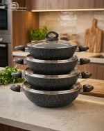 One More black granite non-stick wok set stacked in four sizes (24cm, 26cm, 28cm, 30cm) with glass lids and double handles, featuring a speckled texture for healthy low-oil cooking."
