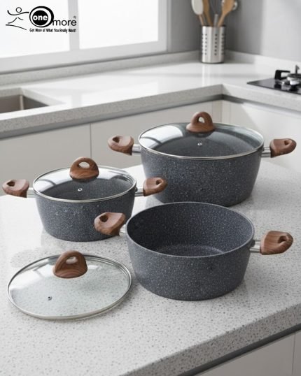 Three-piece One More non-stick granite cooking pot set in grey speckled texture, featuring 24cm, 26cm, and 28cm pots with glass lids and wood-effect silicone handles, displayed on a modern kitchen counter.
