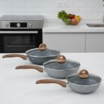 One More grey granite non-stick wok pan with a single long wooden-style handle, cooking shrimp and vegetables on a stove, displaying stone texture.