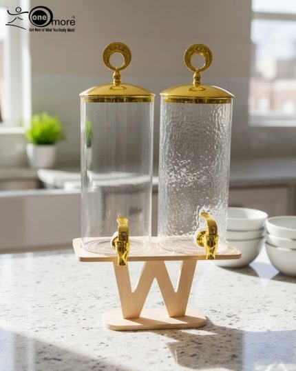 A luxury dual glass beverage dispenser set by One More featuring a 3.3L smooth jar and a 3.3L hammered glass jar, equipped with gold metallic spigots and lids, displayed on a stylish W-shaped wooden stand on a decorated dinner table.