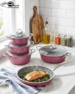 Falez 9-piece purple granite cookware set arranged on a kitchen counter, featuring non-stick deep pots, a shallow casserole with glass lids, and a frying pan with food cooking inside, Made in Turkey.