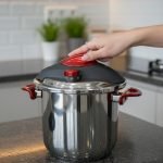O.M.S/ONEMORE 14-liter stainless steel pressure cooker with red handles sitting on a kitchen stovetop, featuring an open lid with steaming hot meat stew inside.
