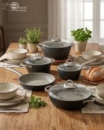 Falez 9-piece black granite non-stick cookware set including fry pan, shallow casserole, and three pots with glass lids and stainless steel handles, arranged on a wooden table.