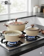 Falez 9-piece beige granite non-stick cookware set arranged on a kitchen surface, featuring three deep pots, one shallow casserole, and one fry pan with wood-effect handles and glass lids, made in Turkey.
