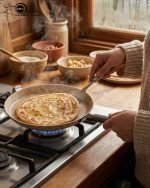 Falez non-stick granite crepe pan in beige speckled finish, shown cooking a golden-brown crepe on a gas stove with a wooden spreader. Option 2: Person flipping a crepe in a Falez granite coated pan, demonstrating non-stick surface and low-oil cooking capabilities.