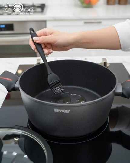 Set of One More non-stick granite casserole pots in 24cm, 26cm, and 28cm sizes with glass lids and ergonomic silicone handles, displayed on a modern kitchen counter.
