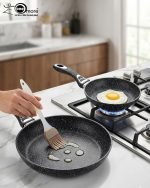 Stack of One More black granite non-stick cooking pots in four sizes (22cm, 24cm, 26cm, and 28cm) with ergonomic handles, displaying a premium speckled texture.