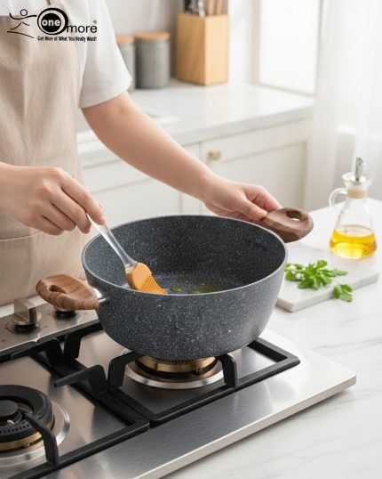 Three-piece One More non-stick granite cooking pot set in grey speckled texture, featuring 24cm, 26cm, and 28cm pots with glass lids and wood-effect silicone handles, displayed on a modern kitchen counter.