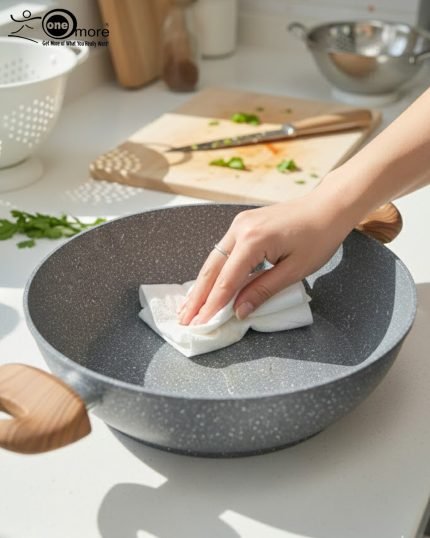 One More grey granite non-stick wok with double handles, stacked in four sizes (24cm, 26cm, 28cm, 30cm) showing stone texture and wooden-style grips on a kitchen counter.