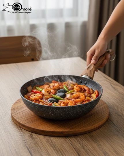 One More grey granite non-stick wok pan with a single long wooden-style handle, cooking shrimp and vegetables on a stove, displaying stone texture.
