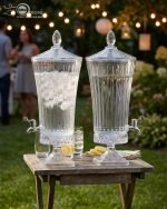 Elegant One More 4.5-liter ribbed glass beverage dispenser filled with orange juice and ice, featuring a silver tap and matching glass lid on a wooden table.
