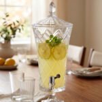 Elegant One More 4.5 liter diamond-cut glass beverage dispenser with a silver spigot and decorative lid, filled with lemon-infused water on a table setting.