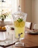 Elegant One More 4.5 liter diamond-cut glass beverage dispenser with a silver spigot and decorative lid, filled with lemon-infused water on a table setting.