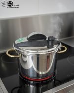 Stainless steel 6-liter pressure cooker with elegant gold handles and black safety locking lid, releasing steam on a stovetop, filled with beef stew – FALEZ kitchenware collection.