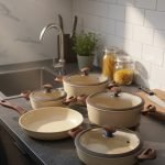 Falez 9-piece beige granite non-stick cookware set arranged on a kitchen surface, featuring three deep pots, one shallow casserole, and one fry pan with wood-effect handles and glass lids, made in Turkey.