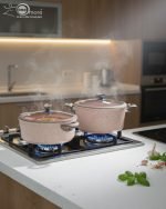 Falez 9-piece pink granite non-stick cookware set including 3 cooking pots with lids, 1 shallow casserole with lid, and 1 frying pan displayed on a kitchen counter and dining table, demonstrating healthy low-oil cooking with steam rising from hot food.