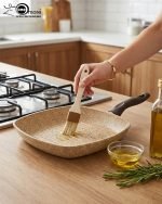 Falez square granite non-stick grill pan cooking grilled chicken breast and vegetables with perfect char marks, featuring a beige speckled finish and ergonomic brown handle.