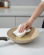 Falez beige granite non-stick wok pan made in Turkey, displayed on a marble kitchen counter with fresh ingredients, showing dynamic stir-fry cooking with shrimp and easy cleaning with a white cloth.