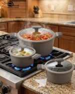 UCC LIFE 9-piece non-stick granite cookware set arranged on a wooden kitchen counter, featuring a frying pan, shallow casserole, and three pots with glass lids in a speckled grey finish.