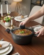Set of One More non-stick granite casserole pots in 24cm, 26cm, and 28cm sizes with glass lids and ergonomic silicone handles, displayed on a modern kitchen counter.