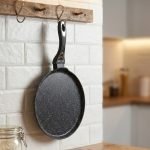 Non-stick 24cm granite crepe pan by One More in black speckled texture, showing a pancake being flipped with a wooden spatula on a gas stove.