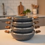 One More grey granite non-stick wok with double handles, stacked in four sizes (24cm, 26cm, 28cm, 30cm) showing stone texture and wooden-style grips on a kitchen counter.