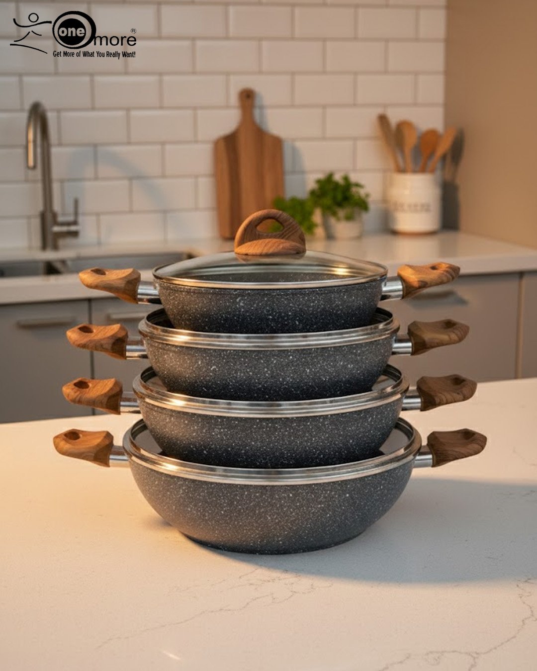 3 One More grey granite non-stick wok with double handles, stacked in four sizes (24cm, 26cm, 28cm, 30cm) showing stone texture and wooden-style grips on a kitchen counter.