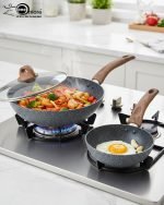 One More grey granite non-stick wok pan with a single long wooden-style handle, cooking shrimp and vegetables on a stove, displaying stone texture.