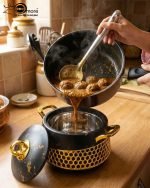 Three One More branded insulated hotpots in black and white marble finishes with gold honeycomb detailing and gold handles, shown in a kitchen and dining room setting with steaming food.