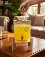 Elegant 5.5L ribbed glass beverage dispenser featuring a gold tap, leather handle, and heart-shaped gold lid knob, displayed on a wooden bamboo stand in a bright, modern dining setting.