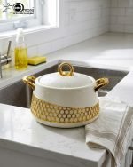 Three-piece luxury insulated hotpot set by One More in matte black and pearl white, featuring gold honeycomb lattice designs, gold handles, and steaming hot food in various dining settings.