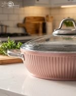 Falez 9-piece pink ceramic granite cookware set featuring a fry pan tossing vegetables, a shallow casserole, and three pots with glass lids, arranged on a kitchen counter and dining table.